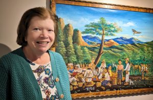Natalie Hartman standing next to a painting of Guatemalan art
