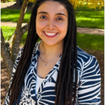 Portrait of Milena Páez Silva smiling outdoors, standing in front of a tree with yellow leaves.